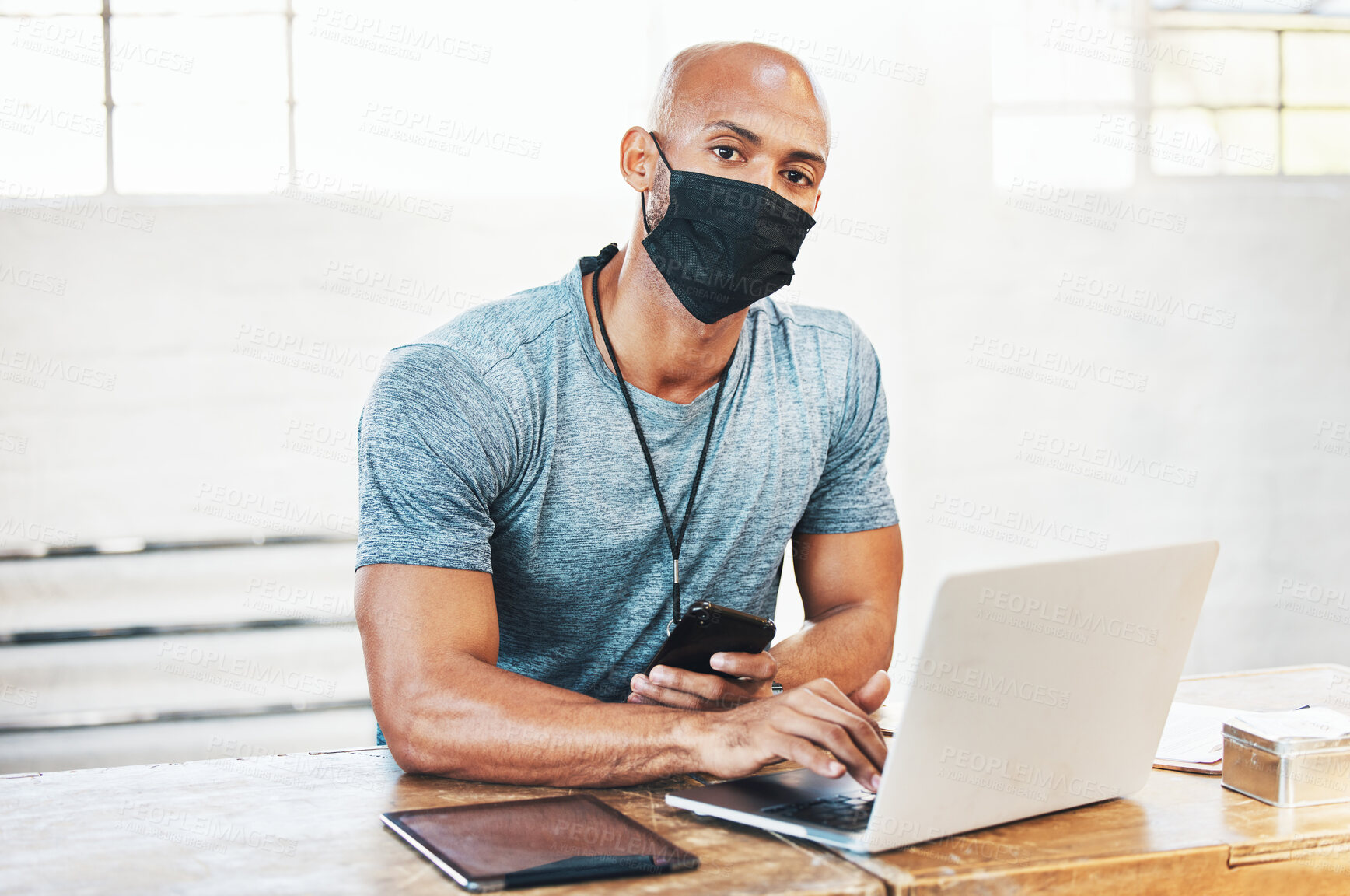 Buy stock photo Portrait of a muscular young man wearing a face mask and using a laptop while working in a gym