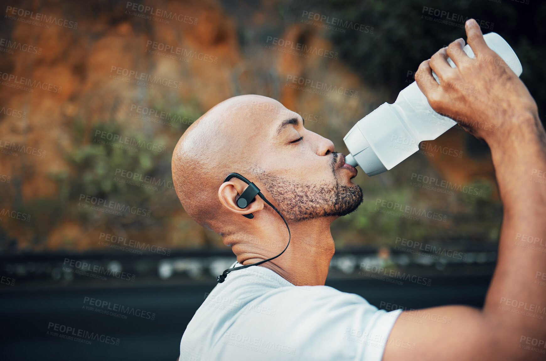 Buy stock photo Man, athlete hydration and outdoor to drink water, profile and earphones for music with exercise. Male person, h2o and cardio break with sports beverage, nutrition and mineral liquid on mountain road