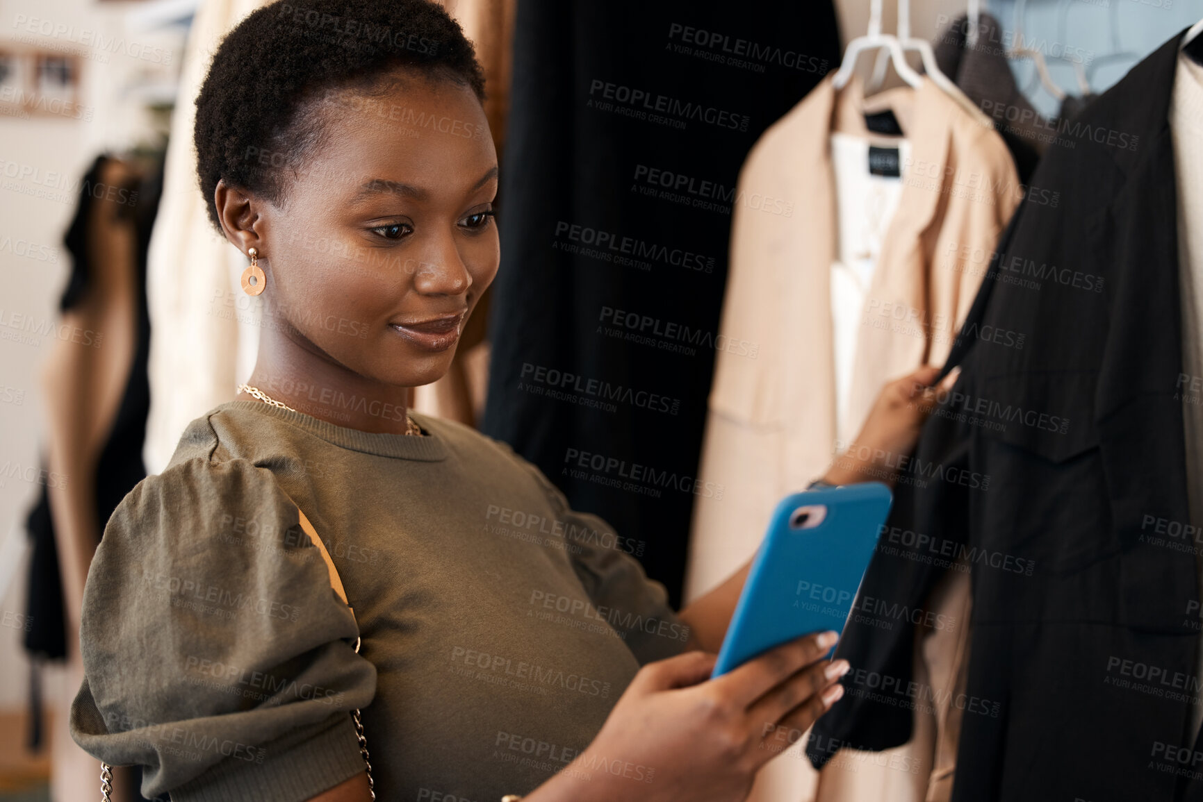 Buy stock photo Shot of a beautiful young woman using her cellphone while shopping for clothing at her favourite boutique