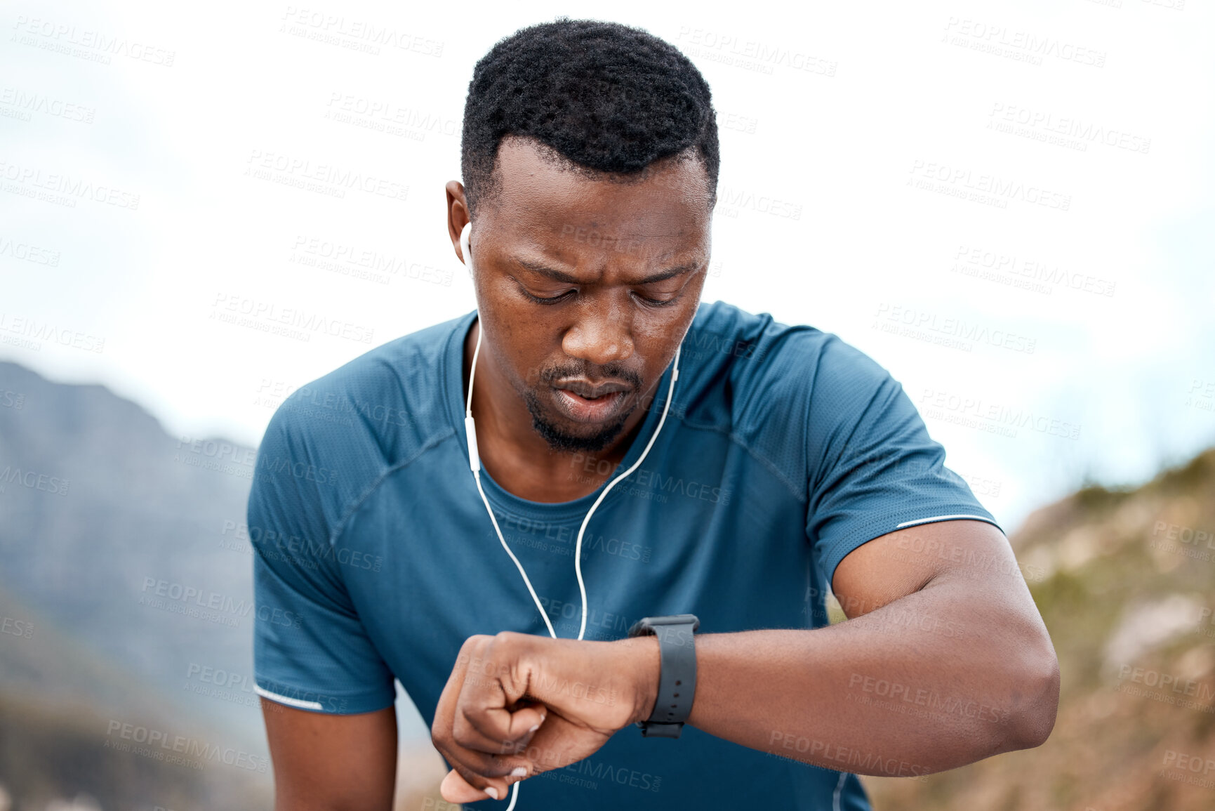Buy stock photo Shot of a sporty young man checking his wristwatch while exercising outdoors