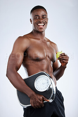 Buy stock photo Studio portrait of a handsome young muscular man posing with a weightscale and apple against a grey background