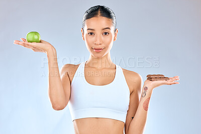 Buy stock photo Woman, portrait and decision with apple or chocolate for diet, choice or options on a blue studio background. Female person, fruit and candy in nutrition, dessert or balance for vitamin or calories