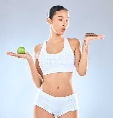 Buy stock photo Woman, choice and pick with apple or chocolate for diet, decision or options on a blue studio background. Female person with fruit and candy for nutrition, dessert or balance for vitamin or calories