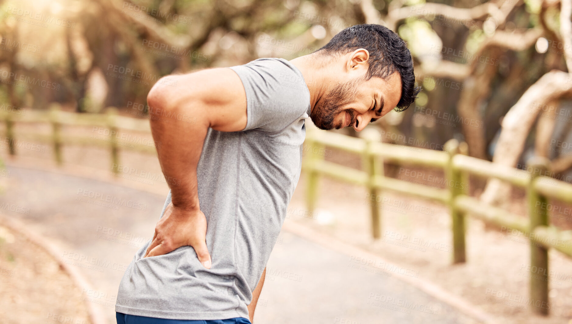 Buy stock photo Shot of a young man experiencing back pain while working out in nature