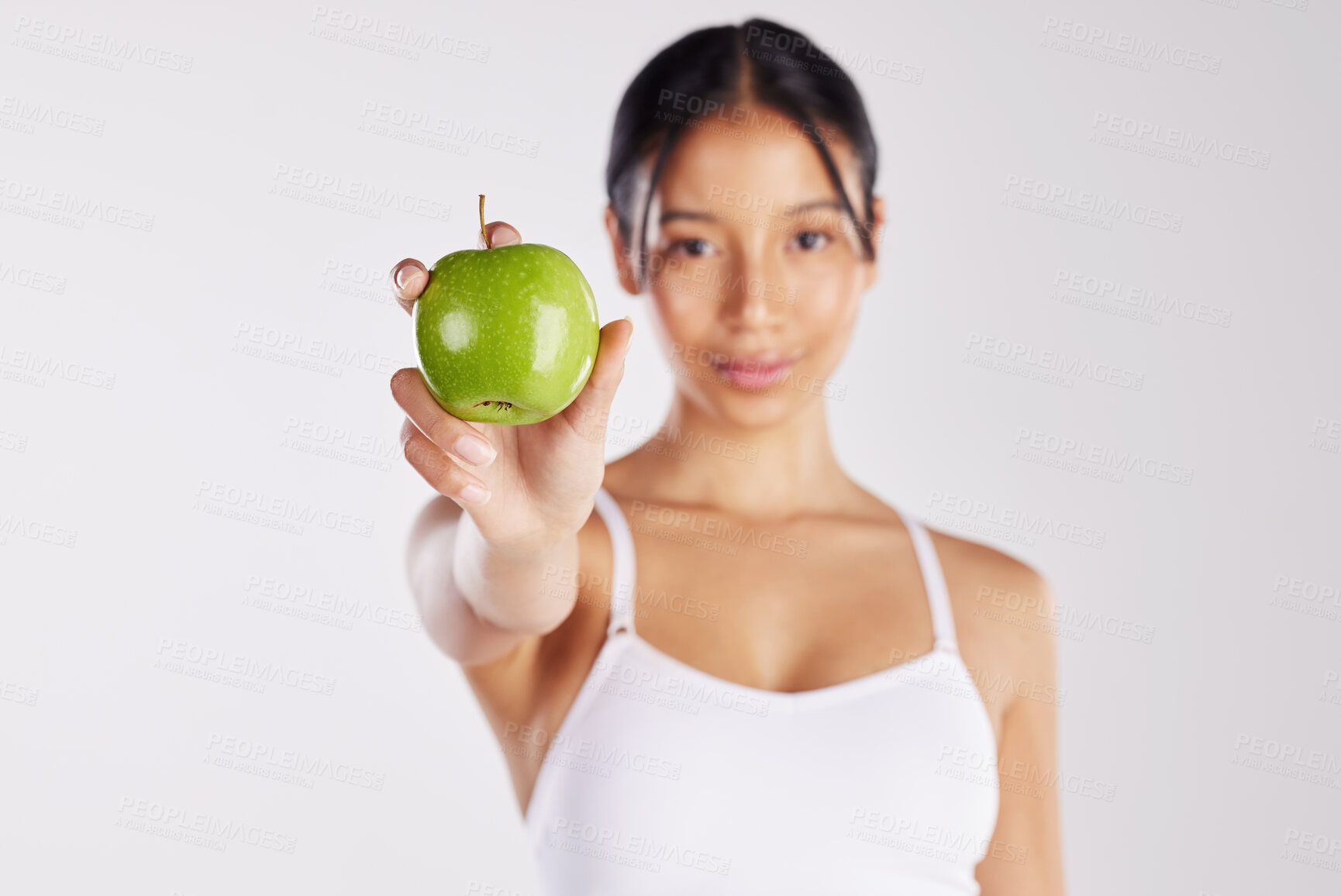 Buy stock photo Shot of a healthy young woman holding an apple while posing against a studio background