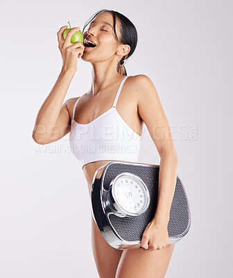 Buy stock photo Shot of a healthy young woman holding an apple and a weight scale