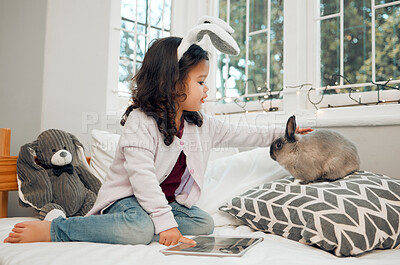 Buy stock photo Child, rabbit and relax in home for love, responsibility and tablet on bed for pet care tutorial. Little girl, bunny or stroke on pillow for trust, development or tech in bedroom for animal education