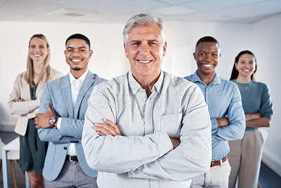 Buy stock photo Portrait of a confident mature businessman standing with his arms crossed in an office with his colleagues behind him