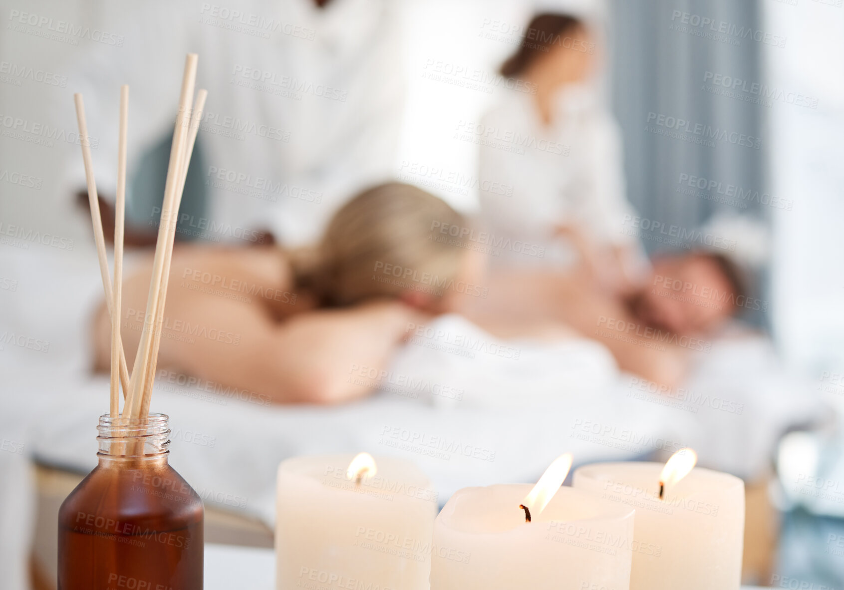 Buy stock photo Shot of some candles and a couple getting a massage in the background in a spa