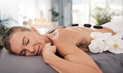 Buy stock photo Spa, hot stone and woman on bed with massage for natural treatment, wellness or stress relief. Resort, body and mature client relax with flower for back therapy, muscle healing, satisfaction