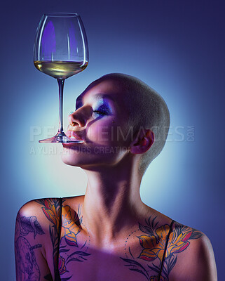 Buy stock photo Studio shot of an attractive young woman wearing edgy makeup and holding a glass of wine in her mouth against a blue background