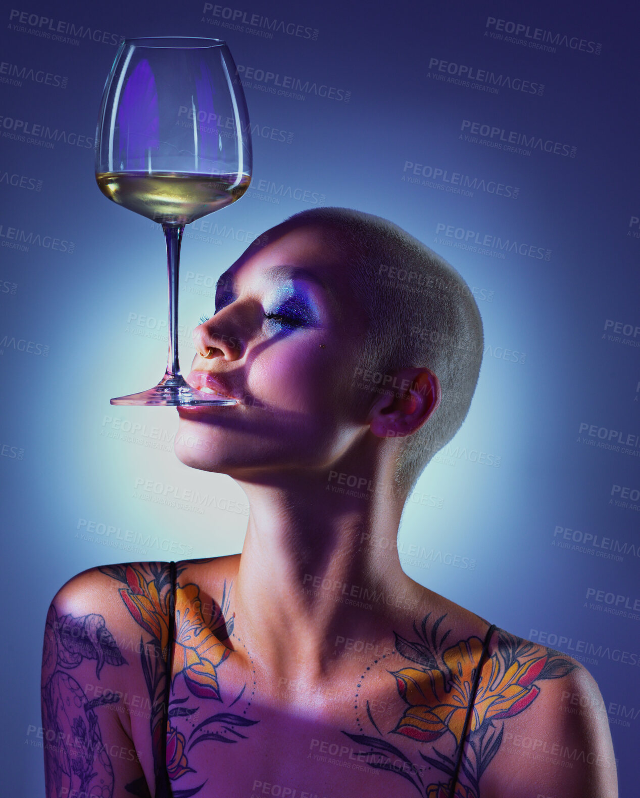 Buy stock photo Studio shot of an attractive young woman wearing edgy makeup and holding a glass of wine in her mouth against a blue background