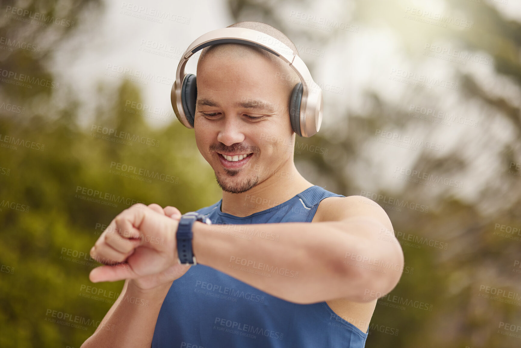 Buy stock photo Shot of a sporty young man wearing headphones and checking his watch while exercising outdoors