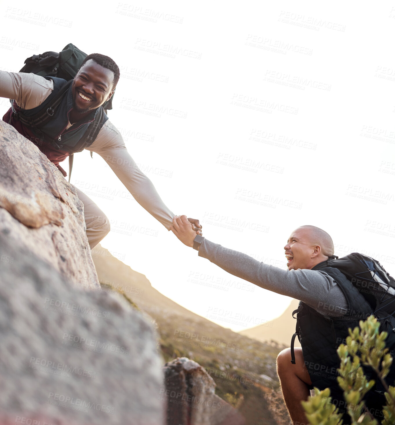 Buy stock photo Cropped shot of a handsome young man helping his friend along a mountain during their hike