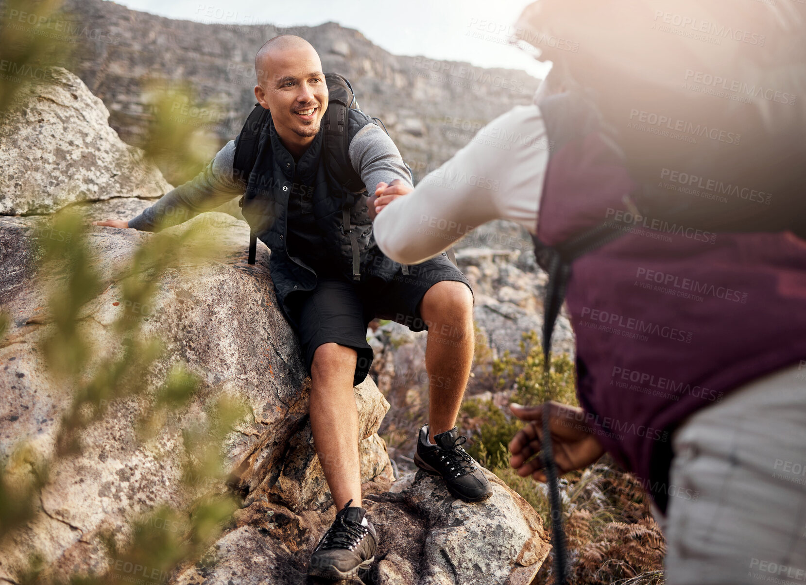 Buy stock photo Cropped shot of a handsome young man helping his friend along a mountain during their hike