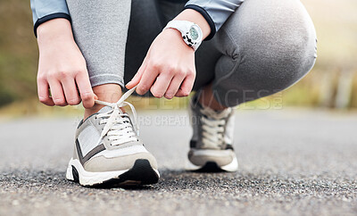 Buy stock photo Cropped shot of a woman tying her shoelaces while out for a run on a road