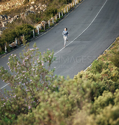 Buy stock photo High angle shot of a woman out for a run on a mountain road