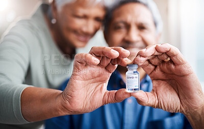 Buy stock photo Shot of a happy senior couple holding the Covid19 vaccine while sitting at home together