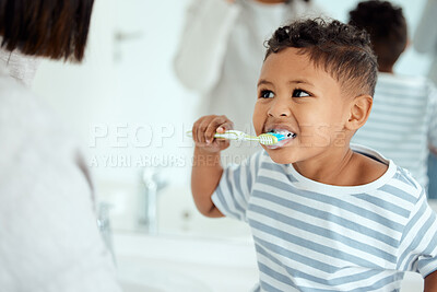 Buy stock photo Shot of an adorable little boy  brushing his teeth while his mother helps him at home