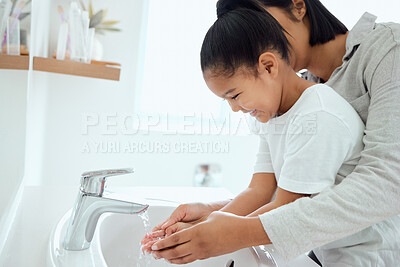 Buy stock photo Shot of an adorable little girl washing her hands while her mother helps at home