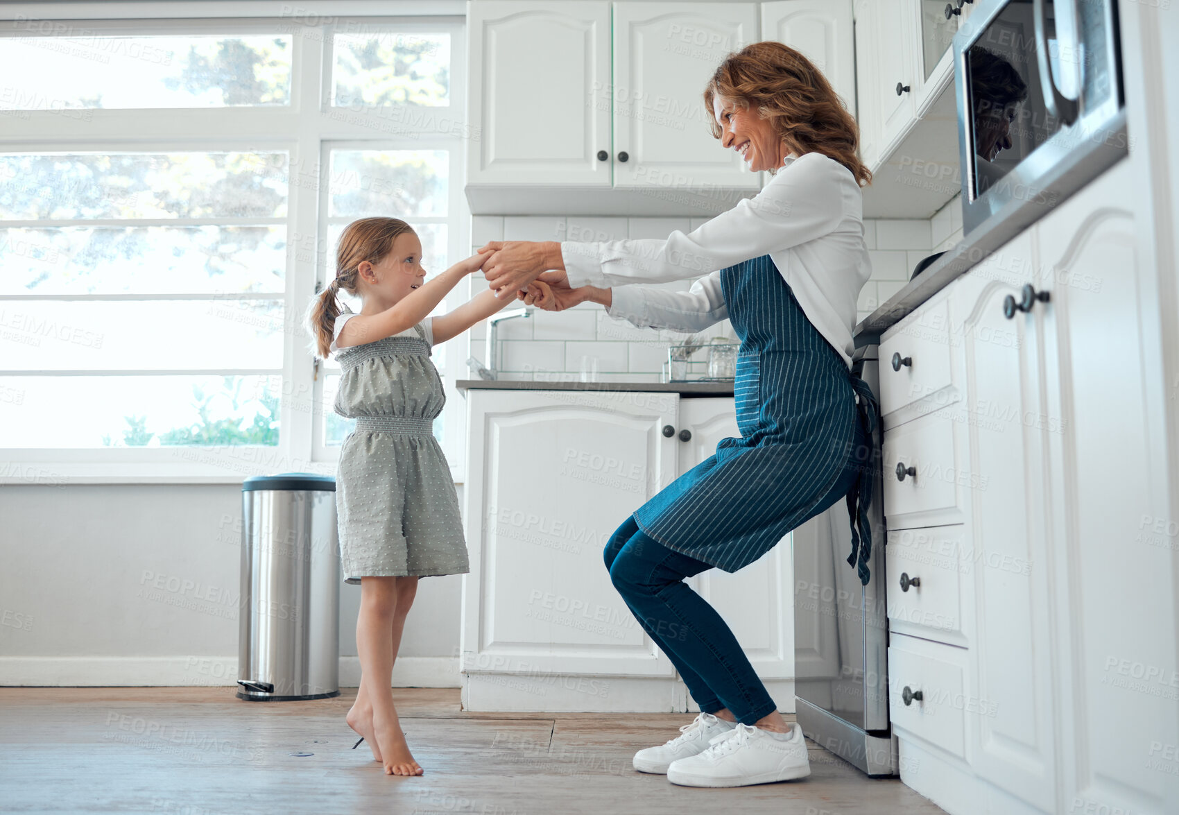 Buy stock photo Shot of a grandmother dancing with her granddaughter in a kitchen at home