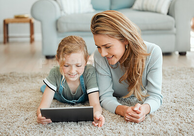 Buy stock photo Shot of an attractive young woman lying on the living room floor with her daughter and using a digital tablet