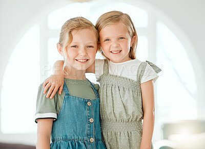 Buy stock photo Shot of two young sisters standing with their arms around each other during a day at home