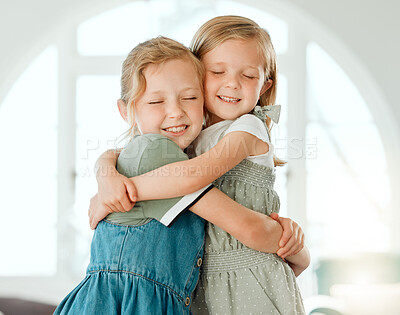 Buy stock photo Shot of two young sisters standing with their arms around each other during a day at home