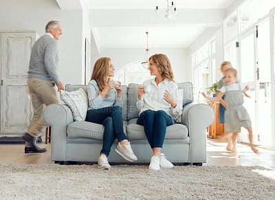 Buy stock photo Shot of a mother and daughter bonding on the couch while the children and grandfather plays a game of chase