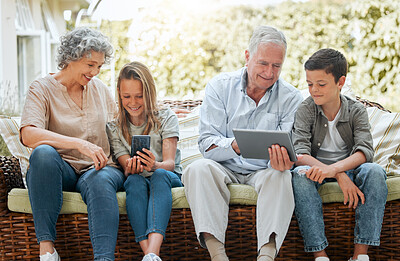 Buy stock photo Shot of a senior couple sitting outside with their grandchildren while using wireless devices