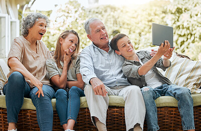 Buy stock photo Shot of a young boy using a digital tablet while sitting at home with his sister and grandparents