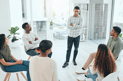 Buy stock photo Shot of a handsome young man standing and talking to his support group