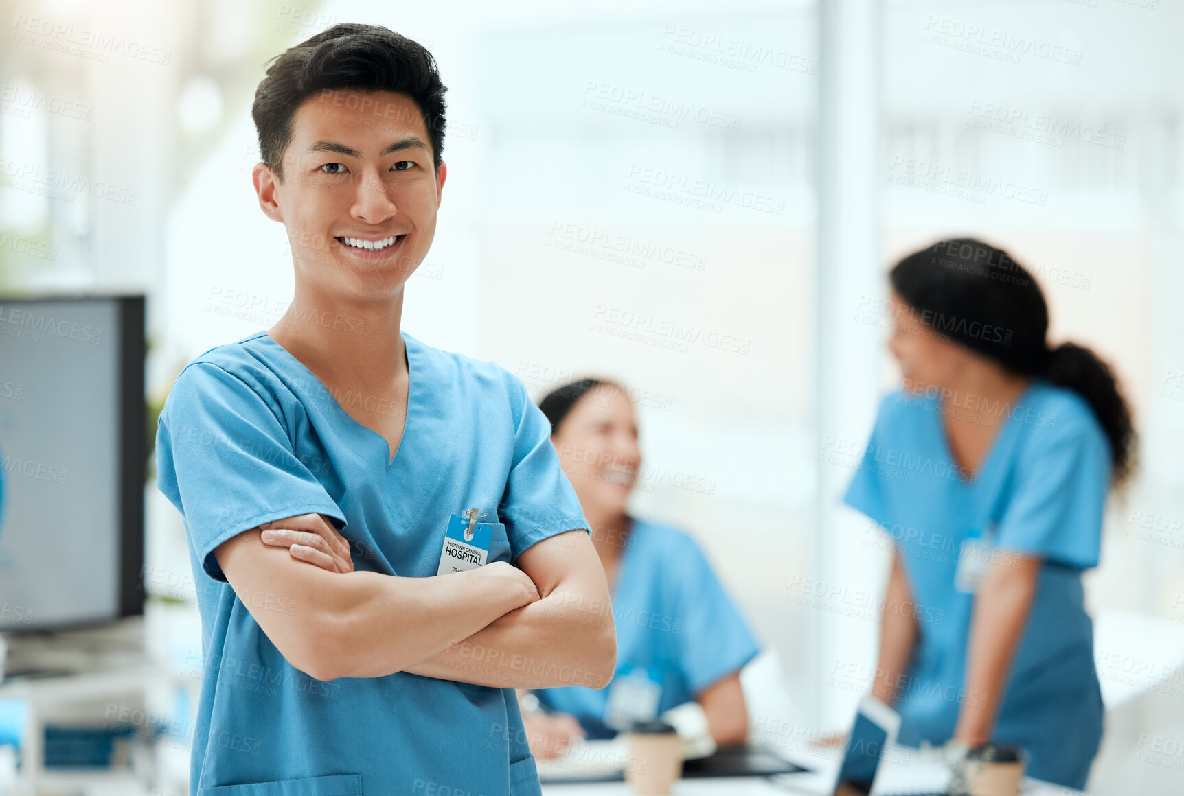 Buy stock photo Shot of a young male doctor standing with his arms crossed at a hospital