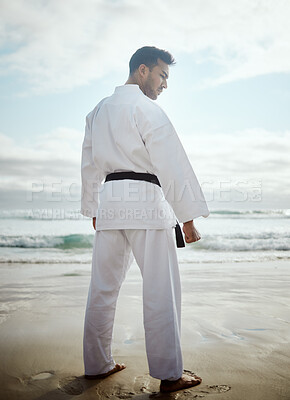 Buy stock photo Rearview shot of a handsome young male martial artist practicing karate on the beach