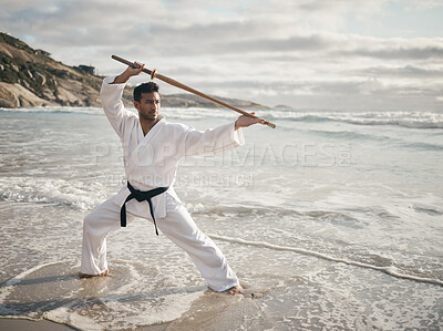 Buy stock photo Full length shot of a handsome young male martial artist practicing karate on the beach