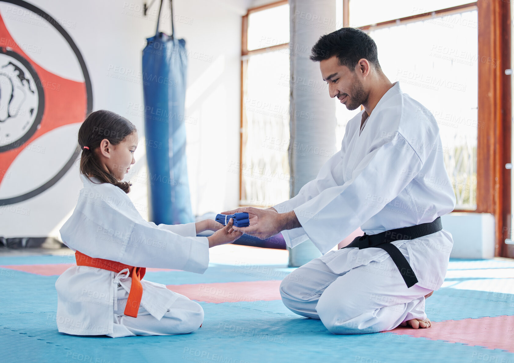 Buy stock photo Karate, promotion and student with blue belt for learning, training and kid practice taekwondo. Martial arts, teacher and people in class for reward, success and master giving girl child obi in gym