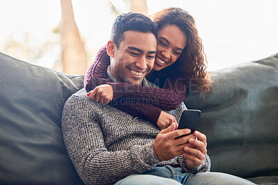 Buy stock photo Happy couple, phone and relax on sofa with social media, internet and online streaming service at home. Young interracial woman and man or partner on video call, connection or hug or love on couch