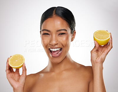 Buy stock photo Studio portrait of an attractive young woman posing with two halves of a lemon against a grey background
