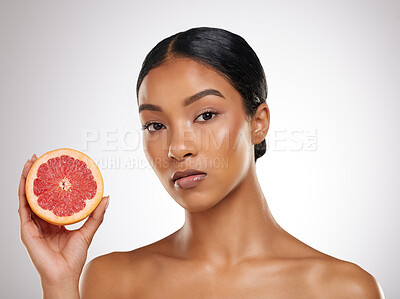 Buy stock photo Studio portrait of an attractive young woman posing with half a grapefrut against a grey background