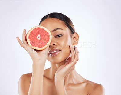 Buy stock photo Shot of a beautiful young woman covering her eye with a grapefruit against a studio background