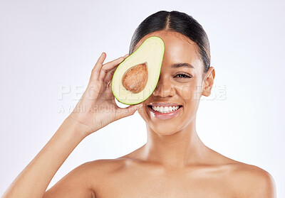 Buy stock photo Shot of a young woman covering her eye with an avocado against a studio background