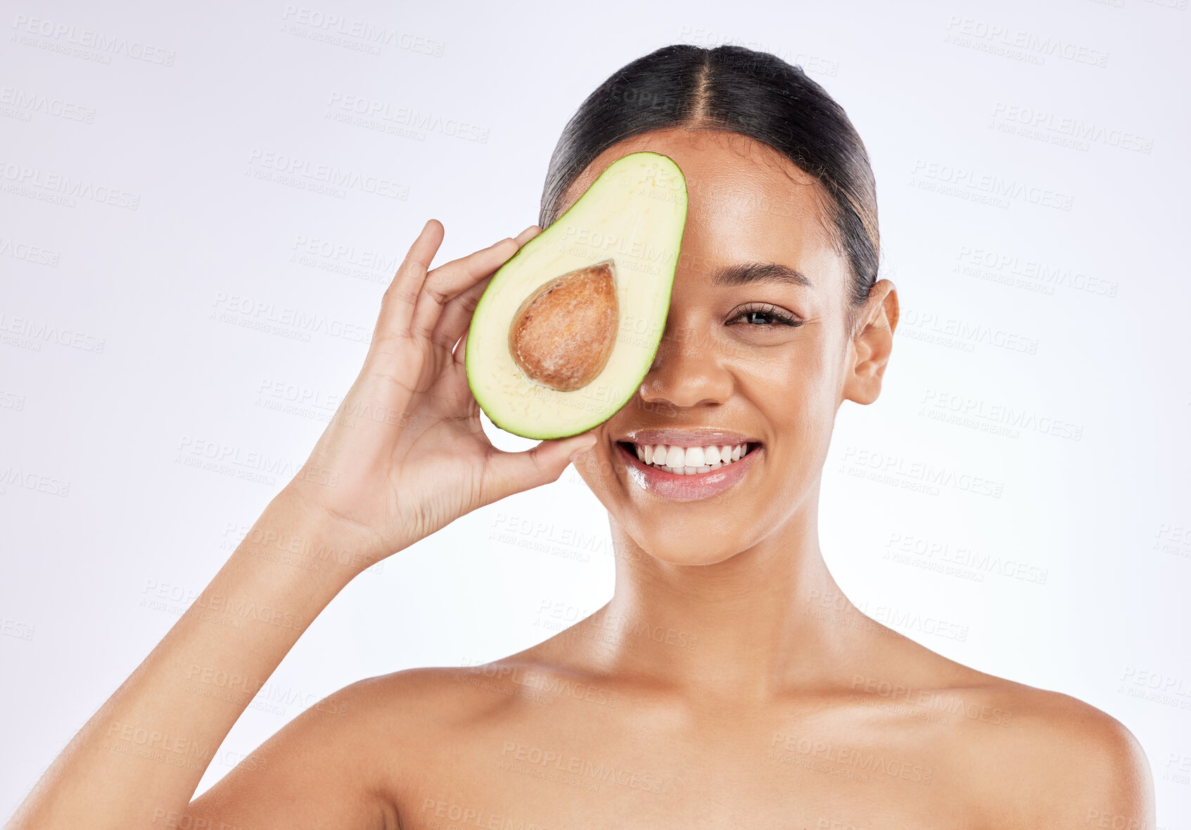 Buy stock photo Shot of a young woman covering her eye with an avocado against a studio background