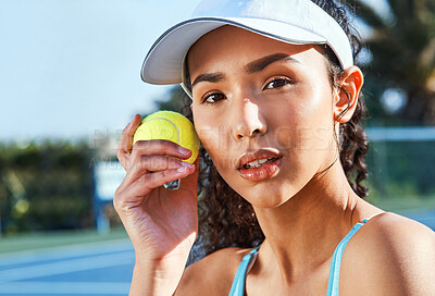 Buy stock photo Shot of an attractive young woman standing and holding a tennis ball while looking contemplative during practice