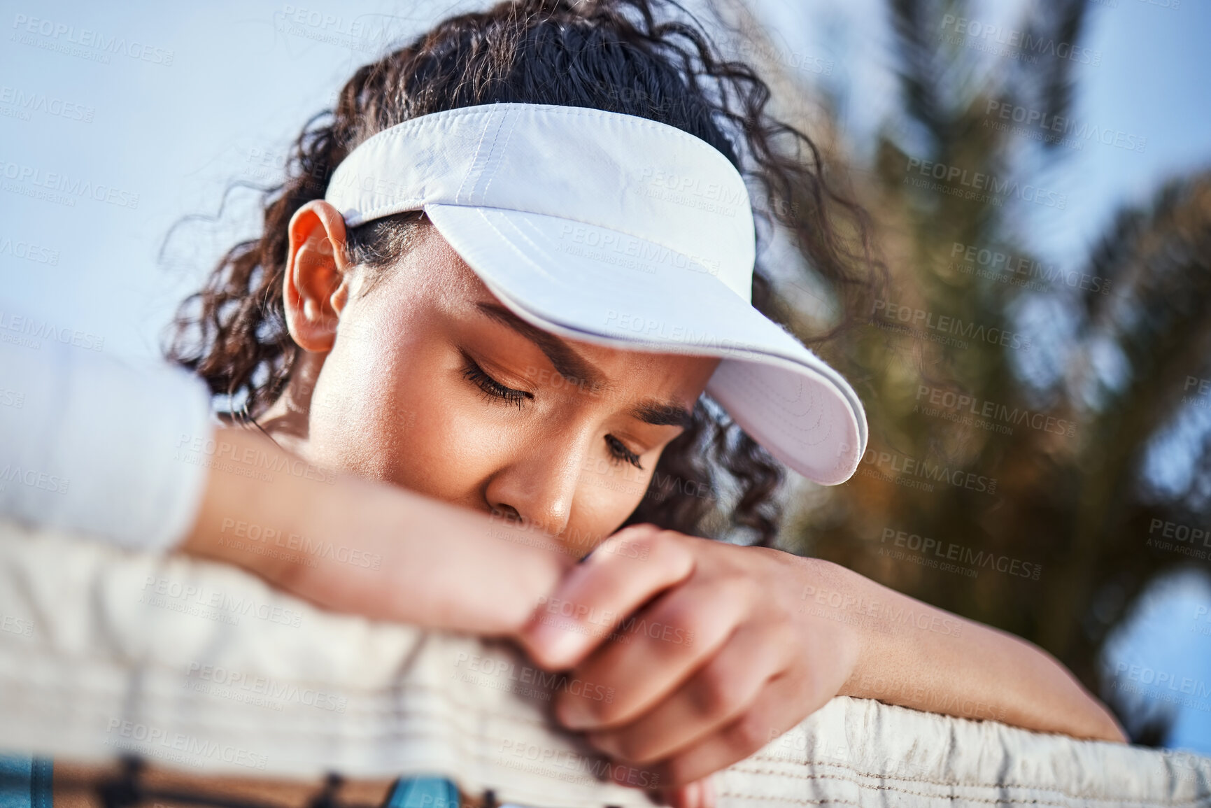 Buy stock photo Shot of an attractive young woman leaning on a tennis net and looking sad after practice