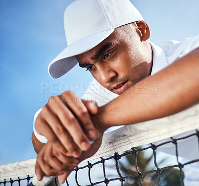 Buy stock photo Shot of a handsome young man leaning on a tennis net and looking disappointed after practice