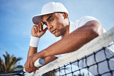 Buy stock photo Shot of a handsome young man leaning on a tennis net and looking disappointed after practice
