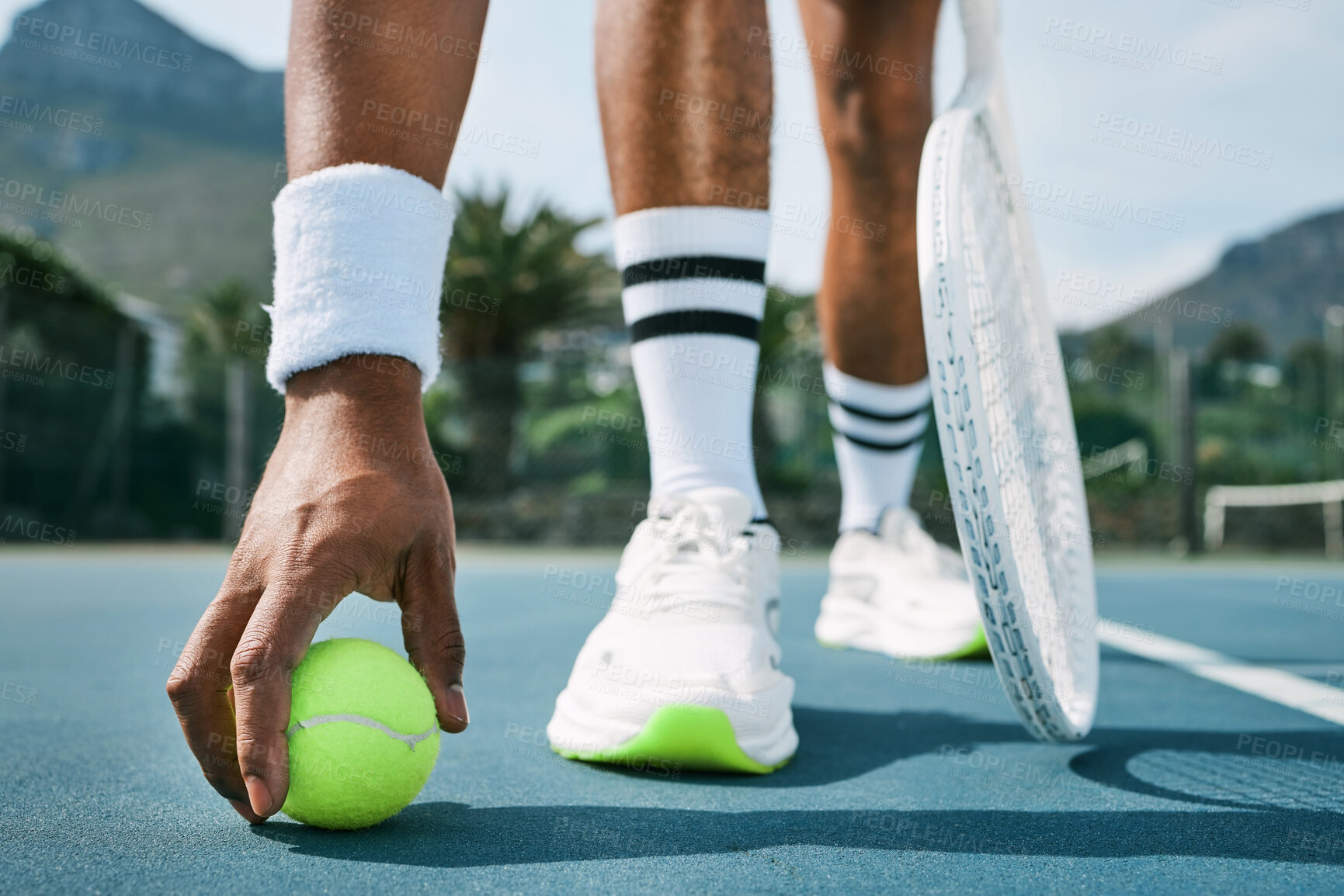 Buy stock photo Cropped shot of an unrecognizable man bending down to pick up a tennis ball during practice