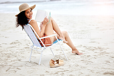 Buy stock photo Shot of a young woman reading a book while relaxing at the beach