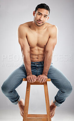 Buy stock photo Studio shot of a handsome young man showing off his muscular body while sitting on a chair against a grey background