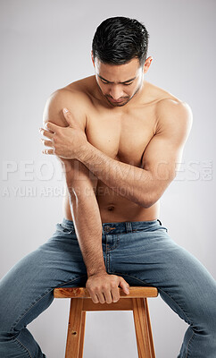 Buy stock photo Studio shot of a handsome young man showing off his muscular body while sitting on a chair against a grey background